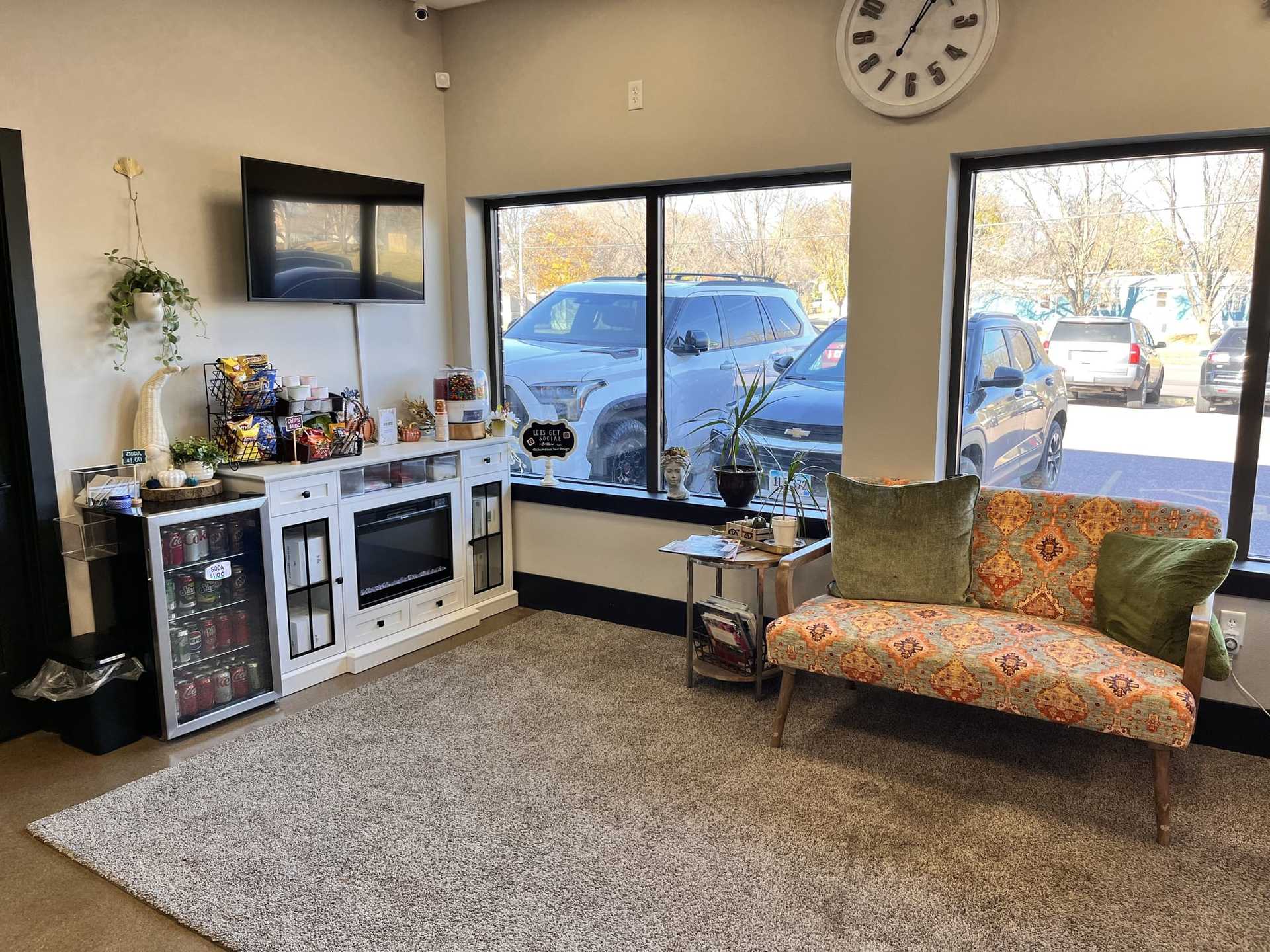 Cozy waiting room with snacks, a TV, couch, and large windows overlooking a parking lot.